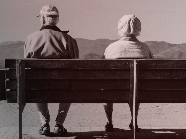 Casal idoso sentado em banco vistos de costas